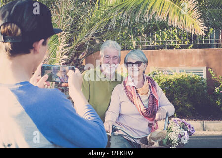 Adolescent avec grands-pères dans une activité de loisirs à prendre des photos avec la technologie de la téléphonie mobile. des profils profiter et sourire la vie. à la fois sur un vieux millésime vélo. l'heure d'été. Banque D'Images