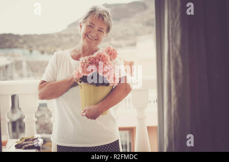 De beaux cheveux blancs âgés de senior woman smile en plein air, sur la terrasse en tenant un vase de fleurs dans le rétroéclairage. accueil concept le bonheur à la retraite de vie Banque D'Images