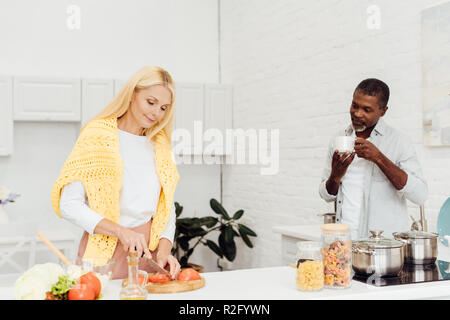 Blonde mature woman cooking dîner pendant african american man drinking coffee Banque D'Images