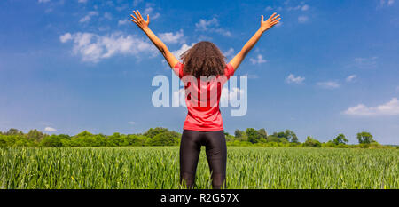 Vue arrière Vue panoramique de bannière web jeune femme fille coureuse jogger debout les bras levés célébrant debout dans green field with blue sky Banque D'Images