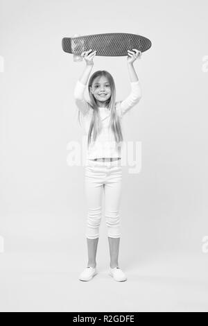 Boy holding skateboard violet au-dessus de sa tête. Champion de course de rue, enfance heureuse concept. Kid en cavalier blanc, jeans et baskets isolé sur fond rose. Enfant avec le joli visage souriant. Banque D'Images