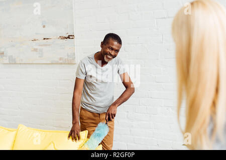 Smiling african american man canapé nettoyage avec duster Banque D'Images