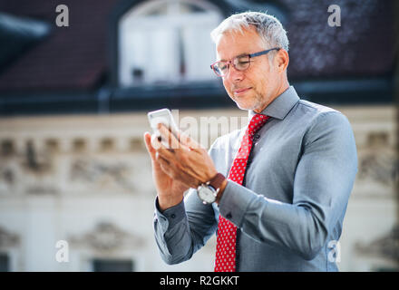 Mature businessman with smartphone debout sur une terrasse en ville, de sms. Banque D'Images