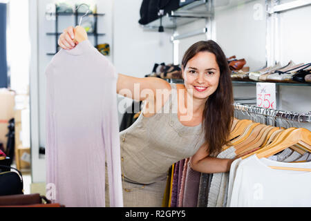 Young happy smiling woman choisir nouveau chemisier à manches longues vêtements en boutique Banque D'Images