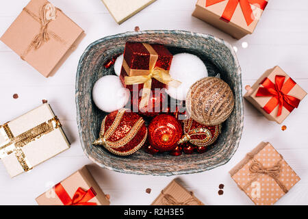 Boîte argentée avec des cadeaux et boules rouges entourés de présente sur fond de bois blanc. Mise à plat. Concept de Noël. Banque D'Images