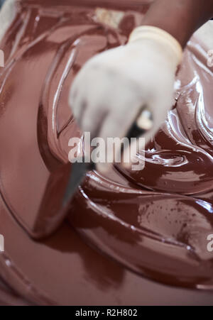 Travailleur de l'usine de confiserie de mélanger le chocolat fondu à l'aide d'une spatule Banque D'Images