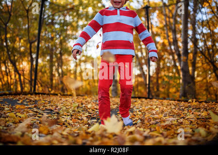 Heureux Garçon sautant sur un trampoline recouvert de feuilles d'automne, United States Banque D'Images