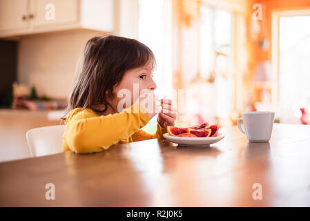 Fille assise à une table en train de manger une orange sanguine Banque D'Images