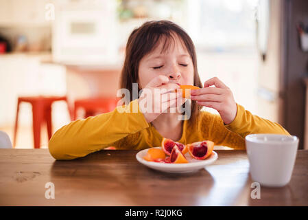 Fille assise à une table en train de manger une orange sanguine Banque D'Images