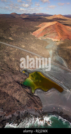 Vue aérienne de la montagne Bermeja, entouré de champs de lave. La route côtière qui traverse les champs de lave noire et un petit lac. Lanzarote, Espagne Banque D'Images