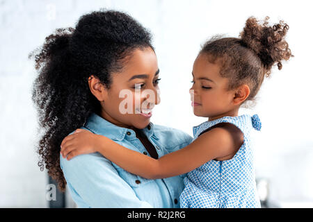 Smiling african american mother and daughter hugging dans la cuisine et à la recherche à l'autre Banque D'Images