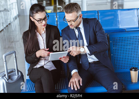 Adult businessman and businesswoman sitting at airport et using digital tablet Banque D'Images