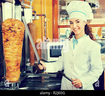 Les jeunes professionnels friendly femme cuisinière avec de la viande grillée sur spit pour kebab Banque D'Images