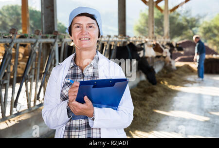 Certains hauts femme vétérinaire avec presse-papiers travaillant sur la ferme de la vache Banque D'Images