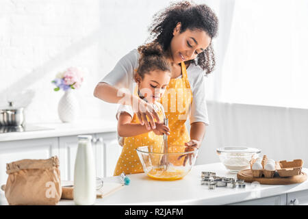 African American mother helping daughter en fouettant les oeufs à la pâte en cuisine Banque D'Images