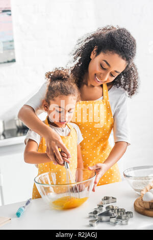 African American mother and daughter en fouettant les oeufs pour la pâte ensemble dans la cuisine Banque D'Images