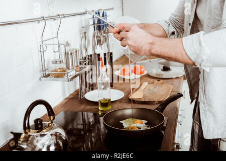 Vue partielle de jeune homme la cuisson des oeufs brouillés au petit déjeuner dans la cuisine Banque D'Images