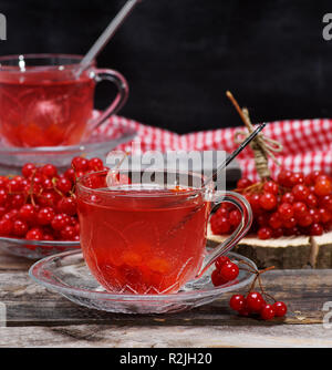 Sex viburnum thé dans une tasse transparente avec une poignée et une soucoupe sur une table en bois gris, à côté de baies fraîches Banque D'Images