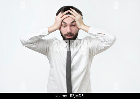 Désespéré, a souligné jeune européen man looking at camera dans la terreur et l'état de choc, holding head Banque D'Images