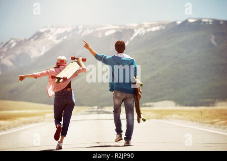 Heureux couple marche par route droite avec skateboards longboards ou sur fond de montagne Banque D'Images