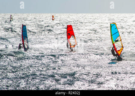 Plusieurs planches à voile dans la baie de Medano au large de la côte de Tenerife sur une surface de l'eau reflétant fortement la lumière du soleil. Banque D'Images