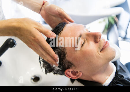 Vue de profil d'un jeune homme de se laver les cheveux et sa tête massés dans un salon de coiffure. Banque D'Images