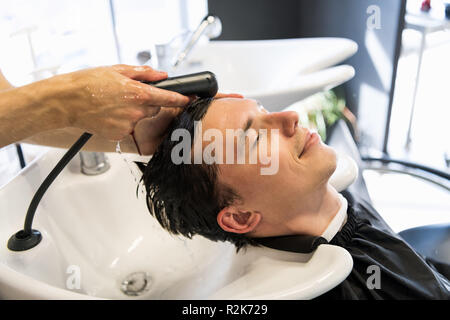 Vue de profil d'un jeune homme de se laver les cheveux et sa tête massés dans un salon de coiffure. Banque D'Images