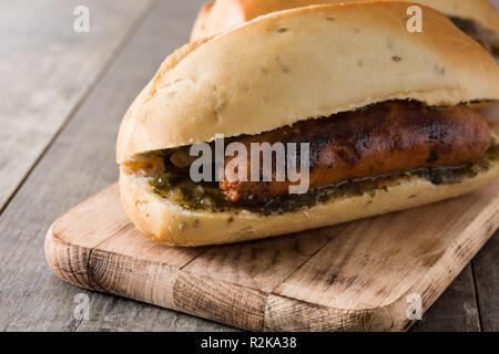 Choripan. L'Argentine traditionnelle avec sandwich chorizo et sauce Chimichurri sur table en bois Banque D'Images