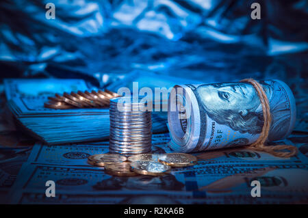 Un rouleau de dollars de pièces de monnaie sur l'arrière-plan d'une centaine de dollars dans la lumière bleue Banque D'Images