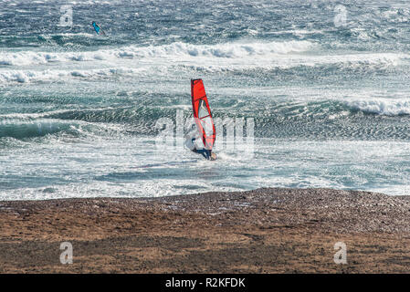 Une planche à voile rouge dans le vent fort en surf un surf. Banque D'Images