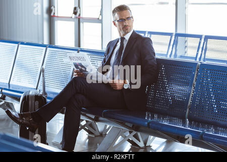 Homme d'adultes dans les verres assis à des départs à l'aéroport et reading newspaper Banque D'Images