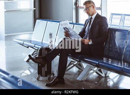 Adult businessman sitting at departure lounge à l'aéroport et reading newspaper Banque D'Images