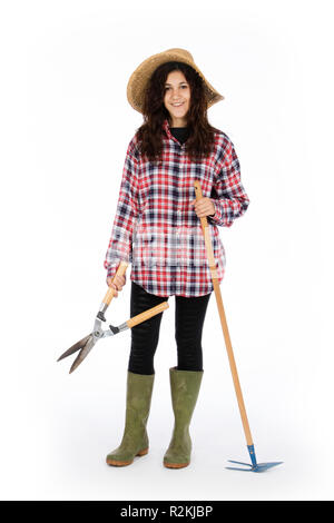 Jeune agriculteur avec cisailles et hoe en mains, elle porte un chapeau de paille, chemise à carreaux et bottes de caoutchouc vert Banque D'Images