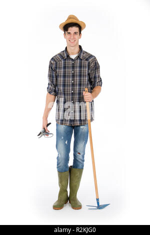 Jeune agriculteur avec cisailles et hoe en mains, il porte un chapeau de paille, chemise à carreaux et bottes de caoutchouc vert Banque D'Images