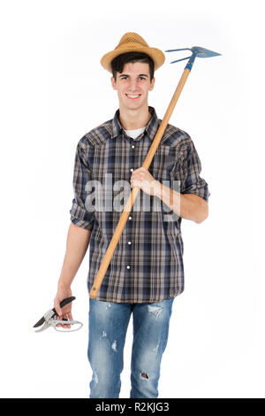 Jeune agriculteur avec cisailles et hoe en mains, il porte un chapeau de paille, chemise à carreaux et bottes de caoutchouc vert Banque D'Images