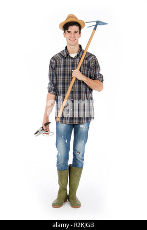 Jeune agriculteur avec cisailles et hoe en mains, il porte un chapeau de paille, chemise à carreaux et bottes de caoutchouc vert Banque D'Images