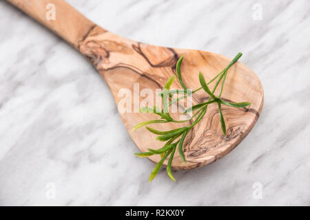 Cuillère en bois avec de faux herbes vert artificiel en elle, sur fond de marbre. Banque D'Images