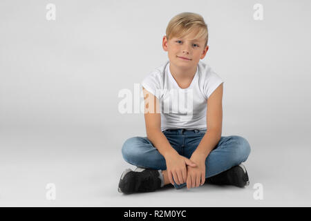 Portrait d'un petit garçon blond est assis en tailleur sur le plancher et de sourires Banque D'Images