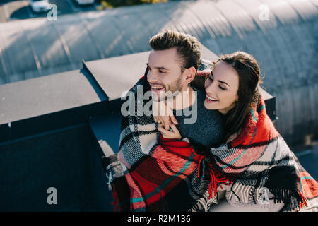 High angle view of laughing young couple sitting on plaid en concert sur le toit Banque D'Images