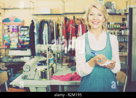 Happy smiling mature woman standing in studio de couture sur mesure prêt à prendre afin Banque D'Images