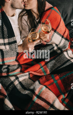 Cropped shot of young couple avec verres de vin blanc et de détente s'embrasser sur la table sous plaid Banque D'Images