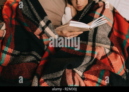 Cropped shot of young woman reading book on couch ensemble plaid sous à la maison Banque D'Images