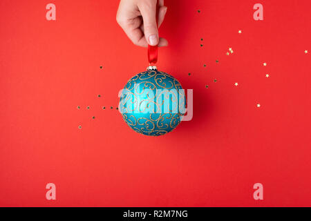 Woman's hand holding Christmas ball émeraude avec des ornements d'or suspendu à un ruban rouge. Carte de vacances de style minimal. Banque D'Images