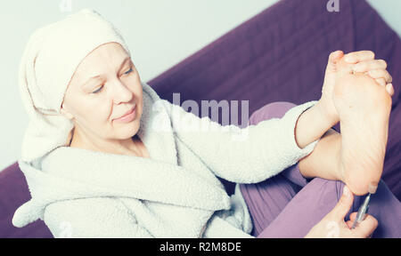 Femme âgée effectuant pédicure avec dispositifs spéciaux à la maison Banque D'Images