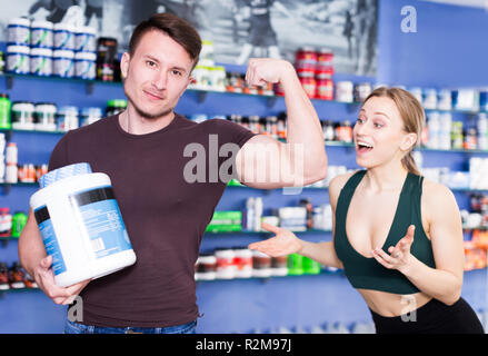 Les personnes gaies athletic avec pot de compléments alimentaires sport démontrant des muscles en intérieur boutique Banque D'Images