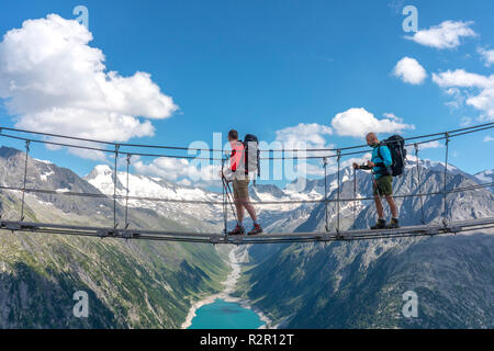 Deux randonneurs sur le pont tibétain près de refuge Olperer avec Schlegeis Stausee sur l'historique, les Alpes de Zillertal, Tyrol, Autriche, district de Schwaz. Banque D'Images