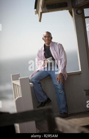 Portrait of a smiling young man holding une tasse de thé sur un balcon. Banque D'Images