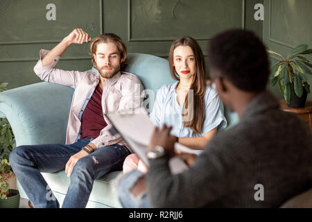 Jeune couple sérieux la visite d'un psychologue assis sur le canapé confortable au cours de session psychologique dans le bureau vert Banque D'Images