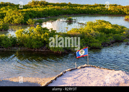 Le pavillon du Belize vole sur un mât de fortune près de San Pedro, Ambergris Caye. Le soleil couchant jette une lueur orange jaune sur la mangrove. Banque D'Images