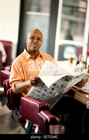 Portrait of a happy Mid adult man lire le journal dans un petit restaurant. Banque D'Images